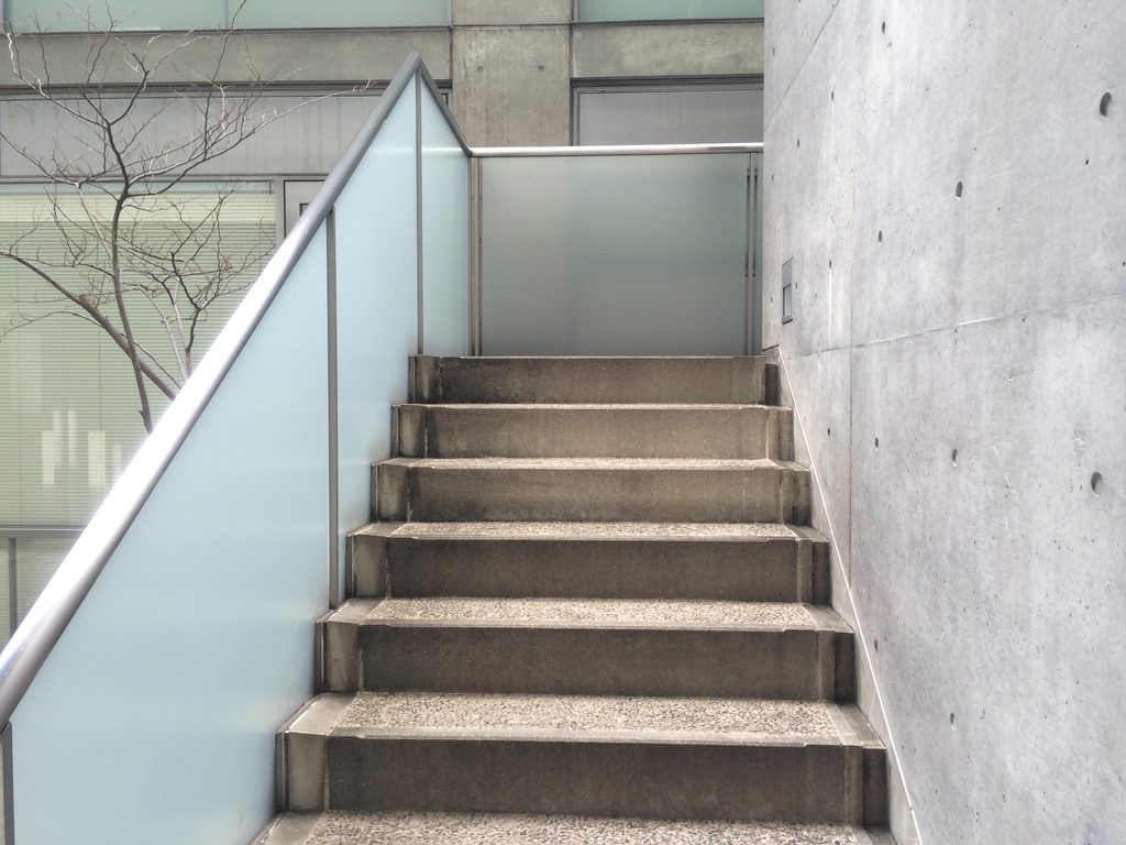コンクリート壁と乳白色ガラスに挟まれたTHE QOLの階段 / Stair between concrete walls and translucent glass at THE QOL