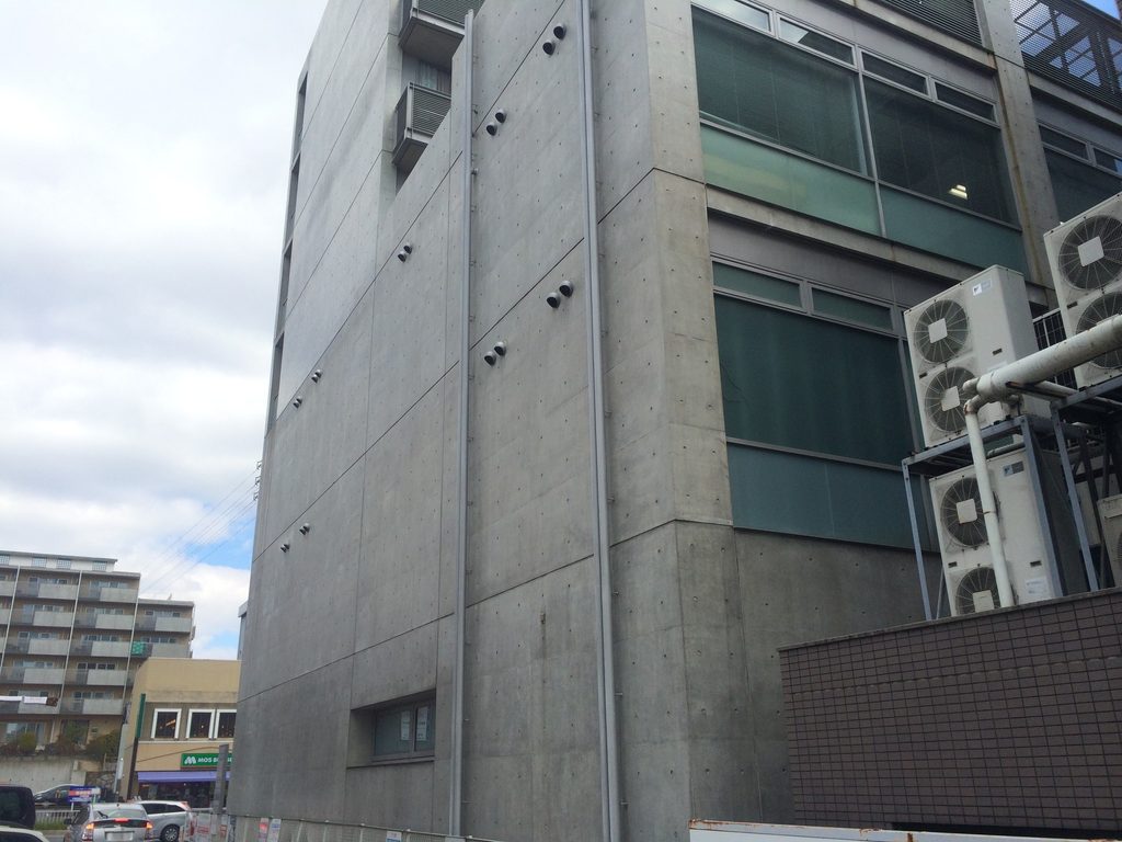 開口を抑えた打放しコンクリート壁が立つTHE QOL側面 / Side elevation of THE QOL dominated by an exposed-concrete wall