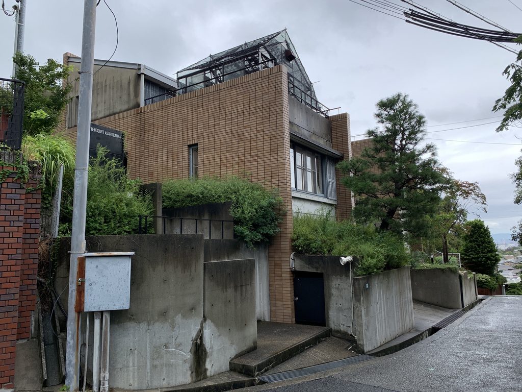 坂道側から見たタイル壁と白い壁面が連なる集合住宅外観 / Residential complex seen from the slope with tiled and white wall surfaces